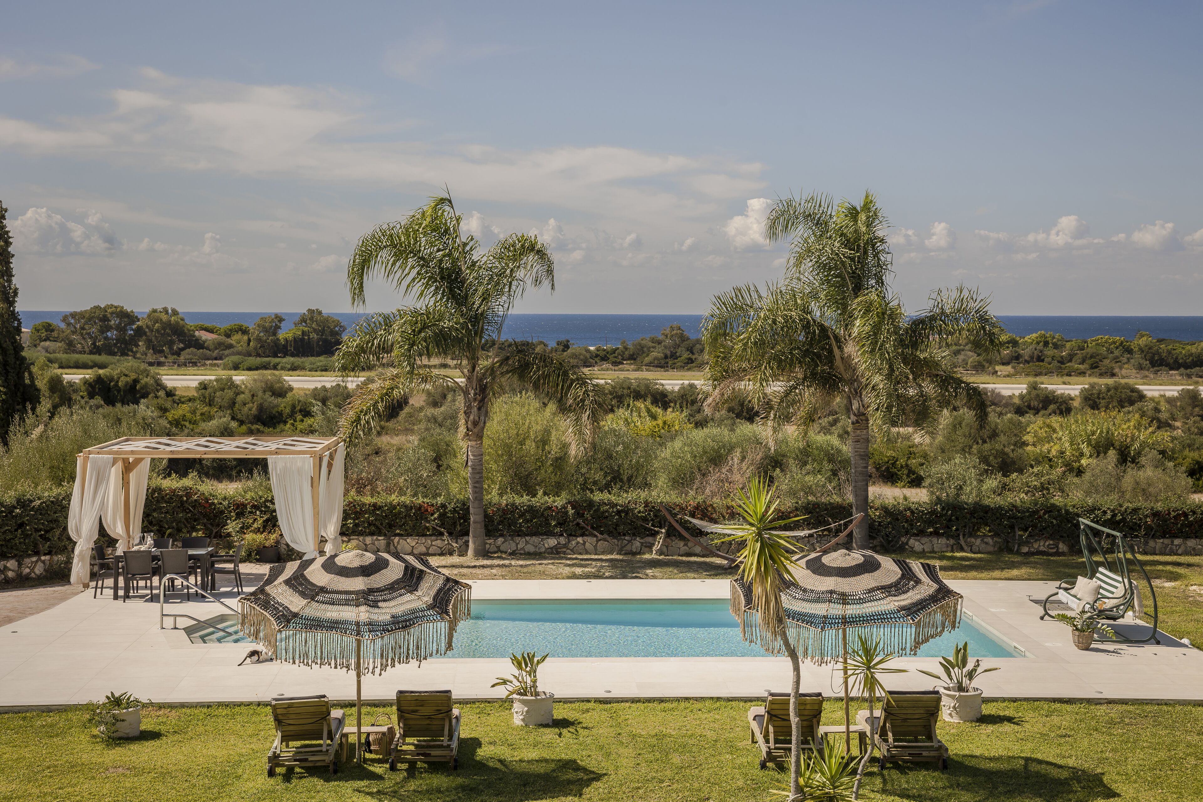 Uma área de piscina com pergolado, cadeiras de descanso e guarda-sóis.