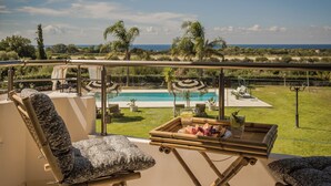 Ein Balkon mit Blick auf einen Pool, Gartenmöbel und eine Platte mit Speisen und Getränken.