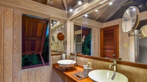 Ein Badezimmer mit Holzvertäfelung, einem großen Spiegel, zwei Waschbecken und einem Fenster mit Blick auf Grünflächen.