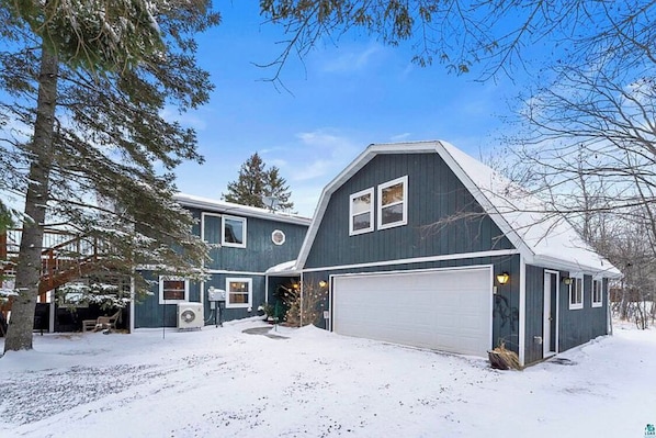 A two-story house with a garage, surrounded by snow-covered ground and trees.