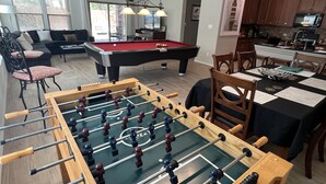 Een woonkamer met een tafelvoetbaltafel, een pooltafel en een eethoek met een tafel gedekt voor vier personen.