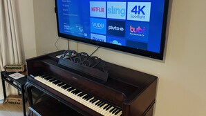 Een televisie aan de wand bevestigd, waarop een Roku-interface met diverse streamingdienstlogo’s te zien is.