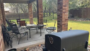 Een overdekt terras met een barbecue, tuinmeubilair en uitzicht op de achtertuin.