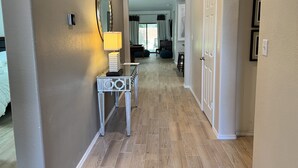 Een gang met een spiegel, een tafel met een lamp en een deur naar een andere kamer.