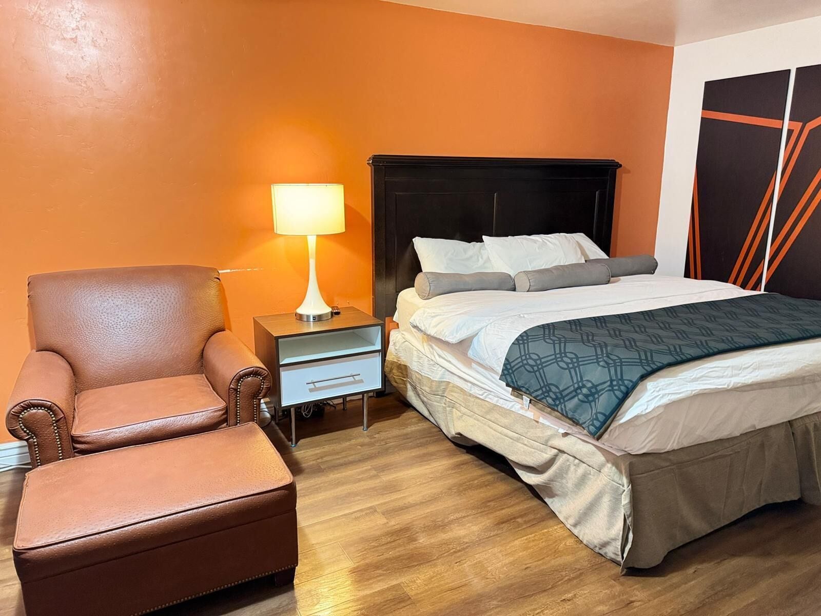 A hotel room with a bed, a chair, a nightstand, and a lamp.