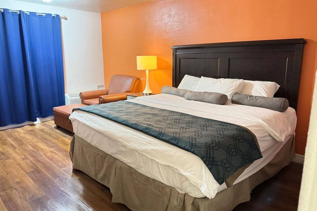 A hotel room with a large bed, a chair, a lamp, and a window with curtains.