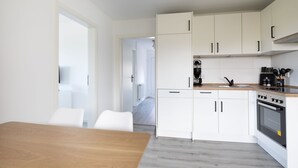 A modern kitchen with white cabinets, a wooden table, and a stove. - Vacation apartment Ankerplatz in House Annika in Schillig-Horumersiel (Wangerland)