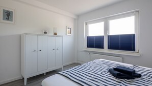 A bedroom with a bed, a wardrobe, a radiator, and a window with blinds. - Vacation apartment Ankerplatz in House Annika in Schillig-Horumersiel (Wangerland)