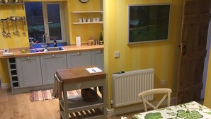 Uma cozinha compacta com pia, armários e radiador. Há uma mesa com toalha e uma cadeira.