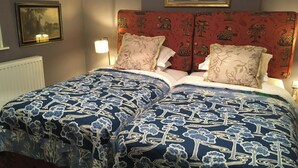 Cama bem arrumada com roupa de cama estampada em flor, cabeceira vermelha e um quadro pendurado acima.