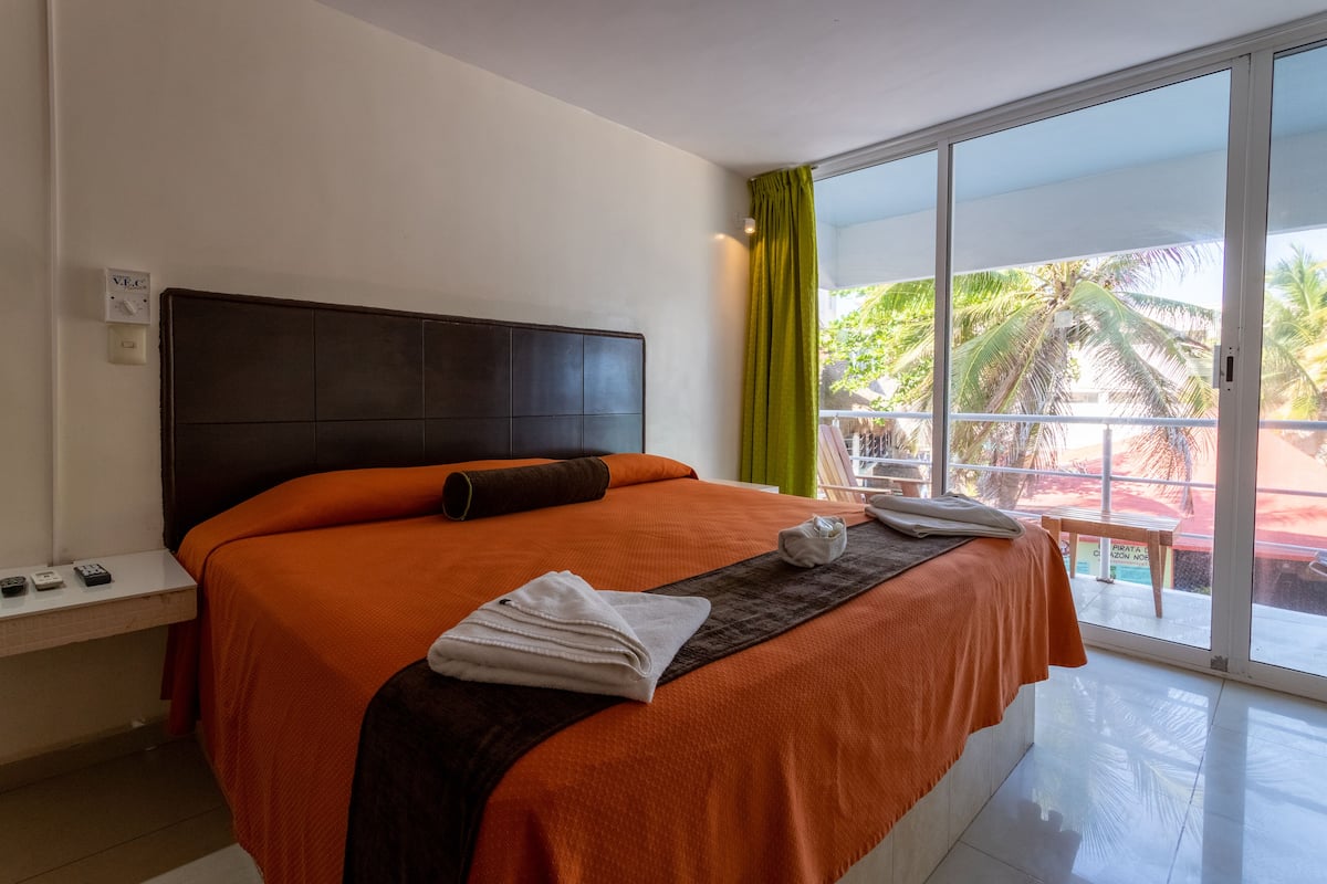 A hotel room with a large bed, a view of palm trees, and a balcony.