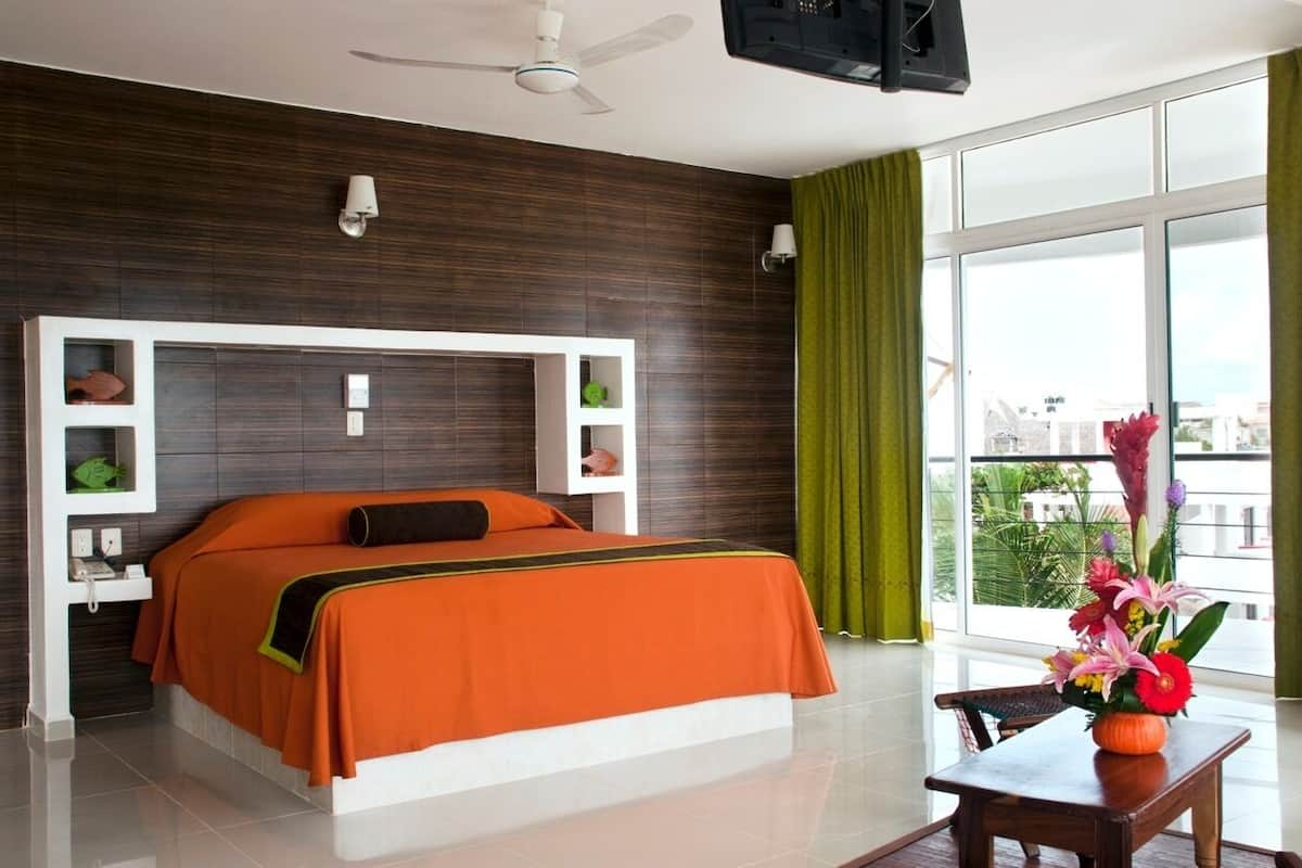 A modern hotel room with a large bed, a flat-screen TV, a ceiling fan, and a balcony with a view.