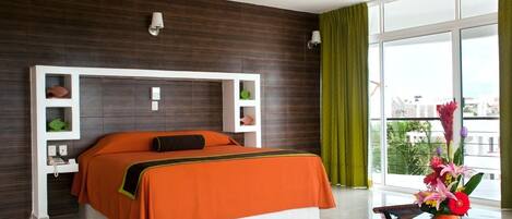 A modern hotel room with a large bed, a flat-screen TV, a ceiling fan, and a balcony with a view.