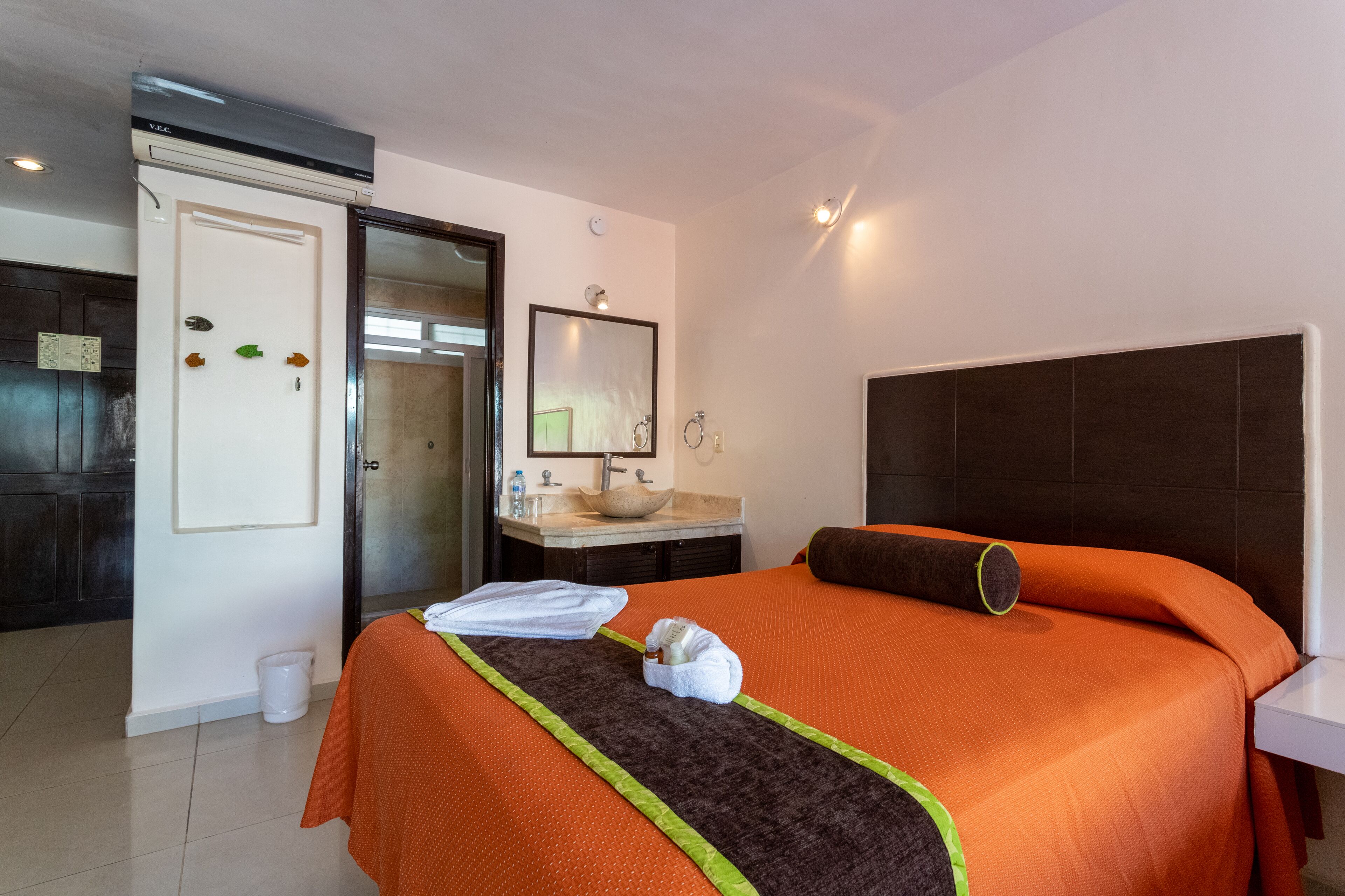 A hotel room with a bed, a bathroom with a sink and mirror, and a door leading to another room.