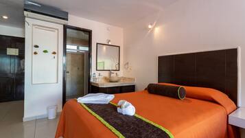 Habitación de hotel con cama, baño con lavamanos y espejo, y una puerta que da a otra habitación.