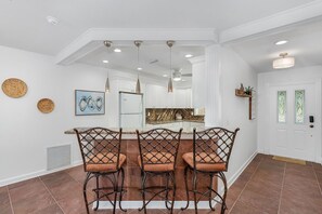 A dining area with a table and four chairs, a kitchen in the background, and a white door with glass panels.