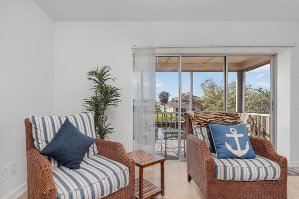 A balcony with wicker furniture, including two chairs and a small table, and a view of the outside.