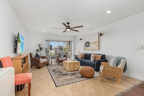 A spacious living room with a ceiling fan, a large TV, a dark sofa, and a wooden coffee table.