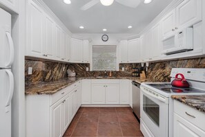 A modern kitchen with white cabinets, a granite countertop, a red kettle, and a microwave.