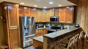 Una cocina moderna con armarios de madera, electrodomésticos de acero inoxidable, encimera de granito y una pared decorativa de piedra.