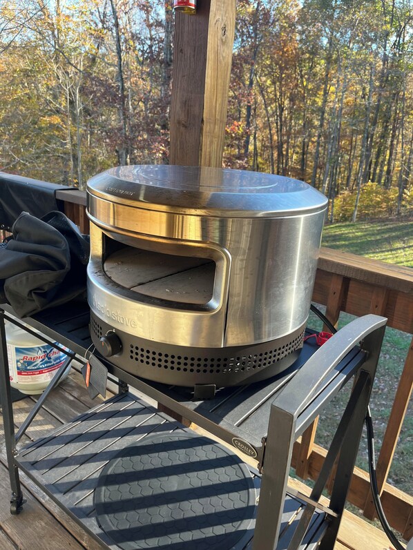 A portable wood stove on a deck with a view of trees in the background.