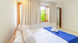 Ein Schlafzimmer mit einem Bett, einem Fenster mit Vorhängen und Blick auf Grün.