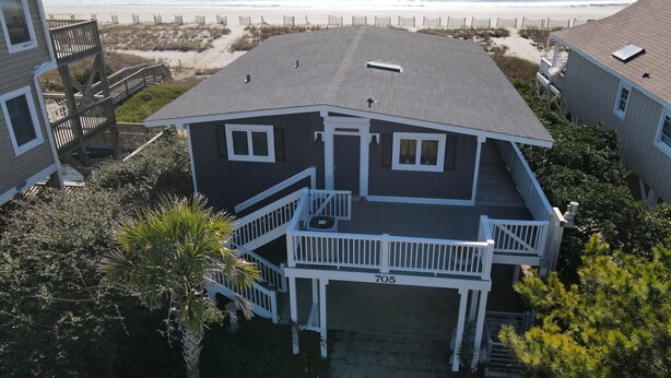 Une maison à deux étages avec un balcon, le numéro « 705 » sur la façade, et une vue sur la plage en arrière-plan.