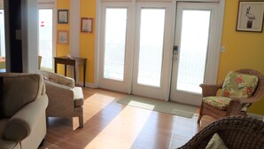 Un salon avec un canapé, un fauteuil et une petite table. Il y a deux portes qui donnent sur l’extérieur.