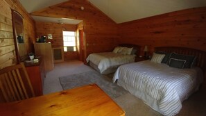 Ein gemütliches Blockhaus-Zimmer mit zwei Betten, einem Holztisch und einer kleinen Küchenzeile.