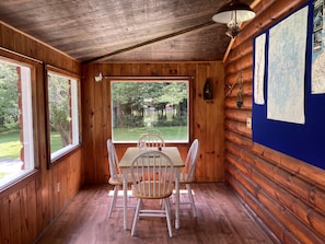 A wooden cabin with a dining table and chairs, large windows, and a map on the wall.