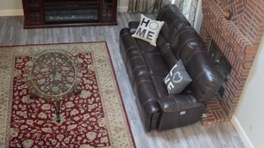 Ein Wohnzimmer mit einer Ledersofa, einem Fernseher, einem Kamin und einem gemusterten Teppich.