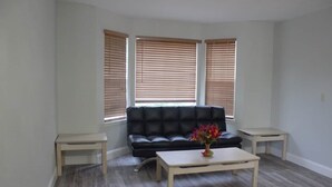 Ein Wohnzimmer mit einem schwarzen Ledersofa, zwei kleinen Beistelltischen, einem Couchtisch und einer Vase mit Blumen.