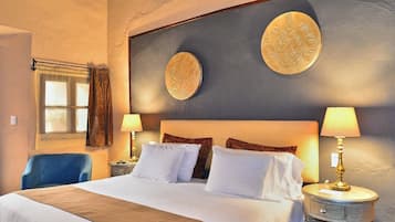Habitación de hotel con una cama grande, dos lámparas de noche, una silla y un ventanal con cortinas.
