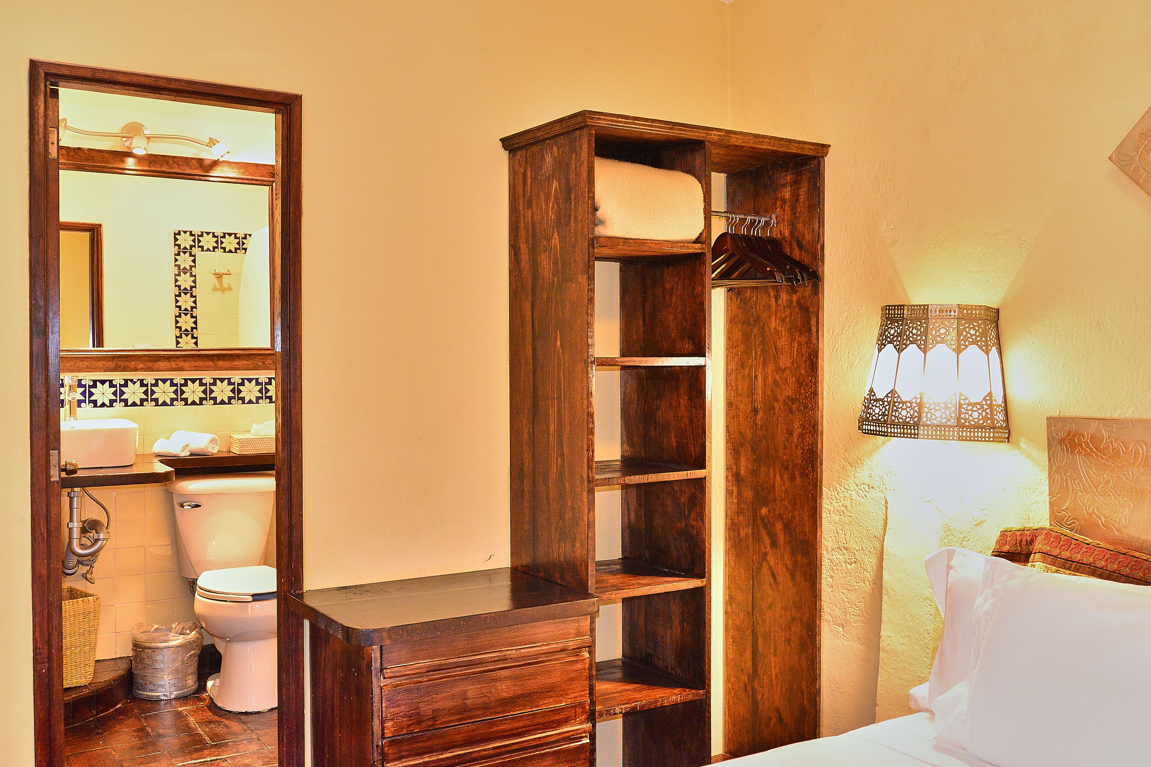 A bathroom with a wooden vanity, a toilet, a mirror, and a wall-mounted lamp.
