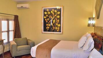 Quarto de hotel com uma cama, uma cadeira, ar condicionado fixado na parede, um quadro emoldurado e uma luminária na parede.