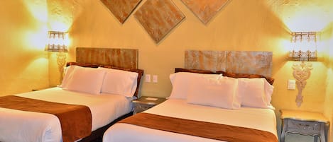 Habitación de hotel con dos camas, cada una con cabecera de madera, ropa de cama blanca y manta marrón. Hay lámparas de pared a ambos lados de las camas.