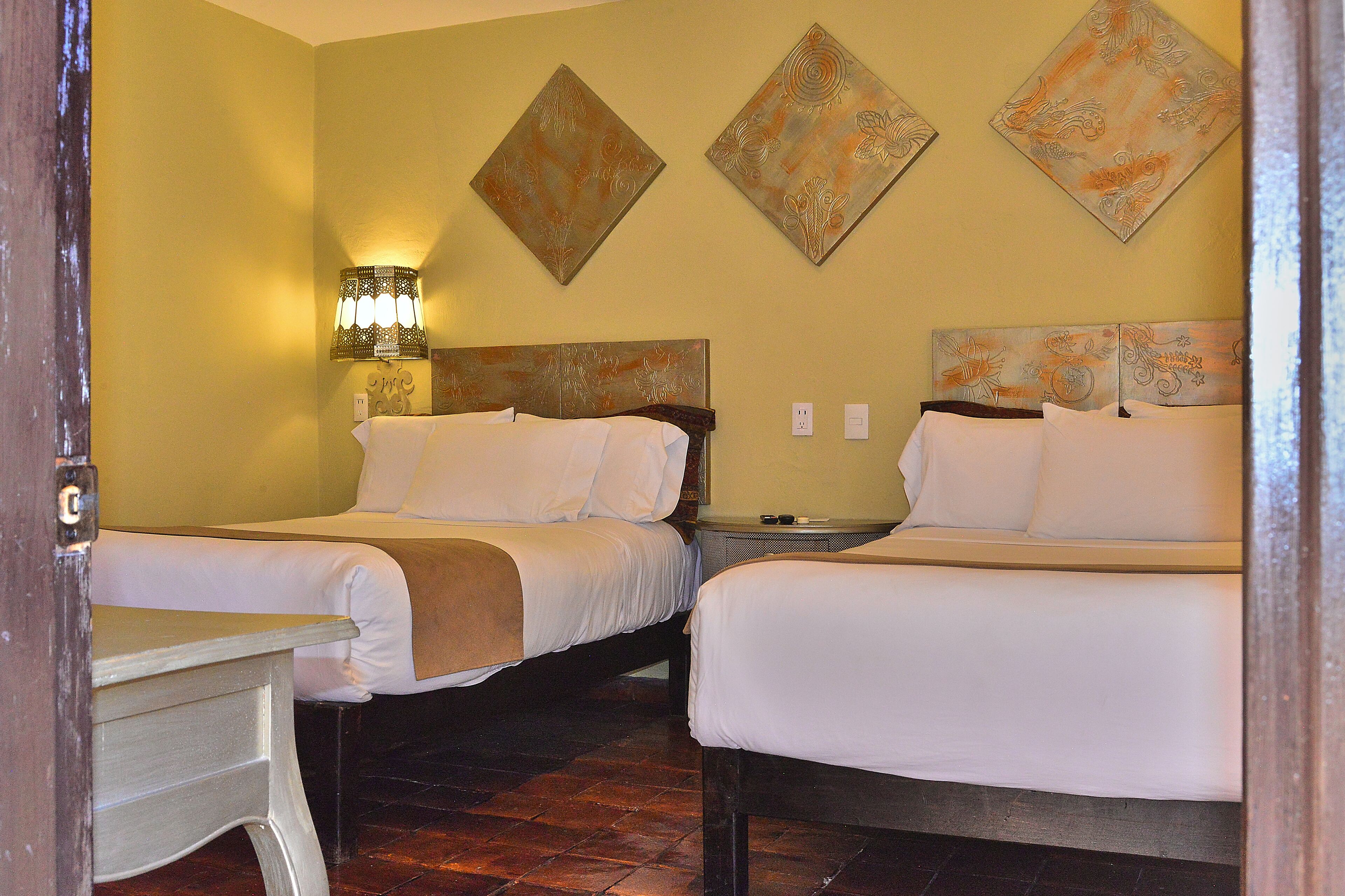 Habitación de hotel con dos camas, una mesita de noche, una lámpara y obras de arte en las paredes.