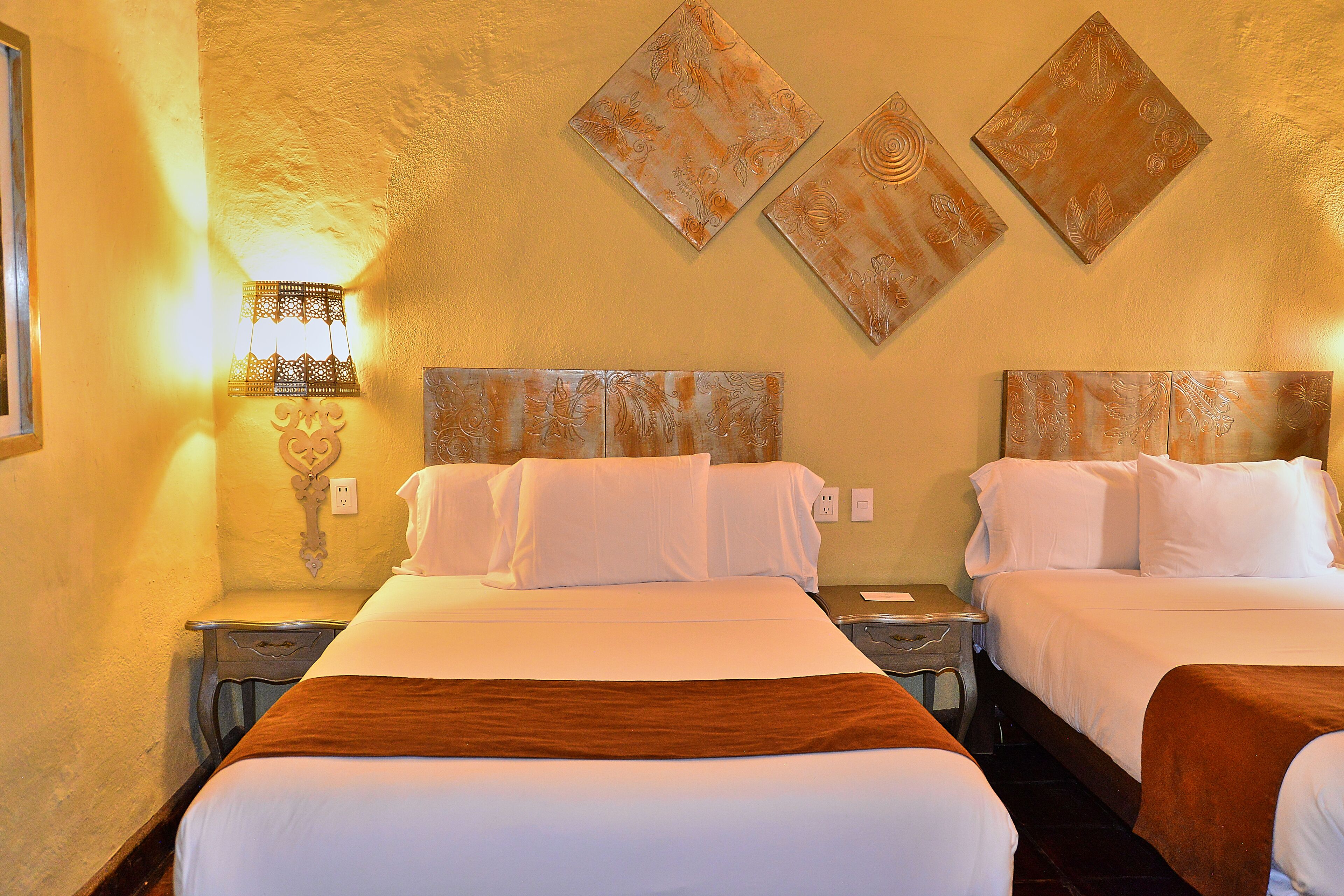 A hotel room with two beds, a nightstand with a lamp, and wall art.