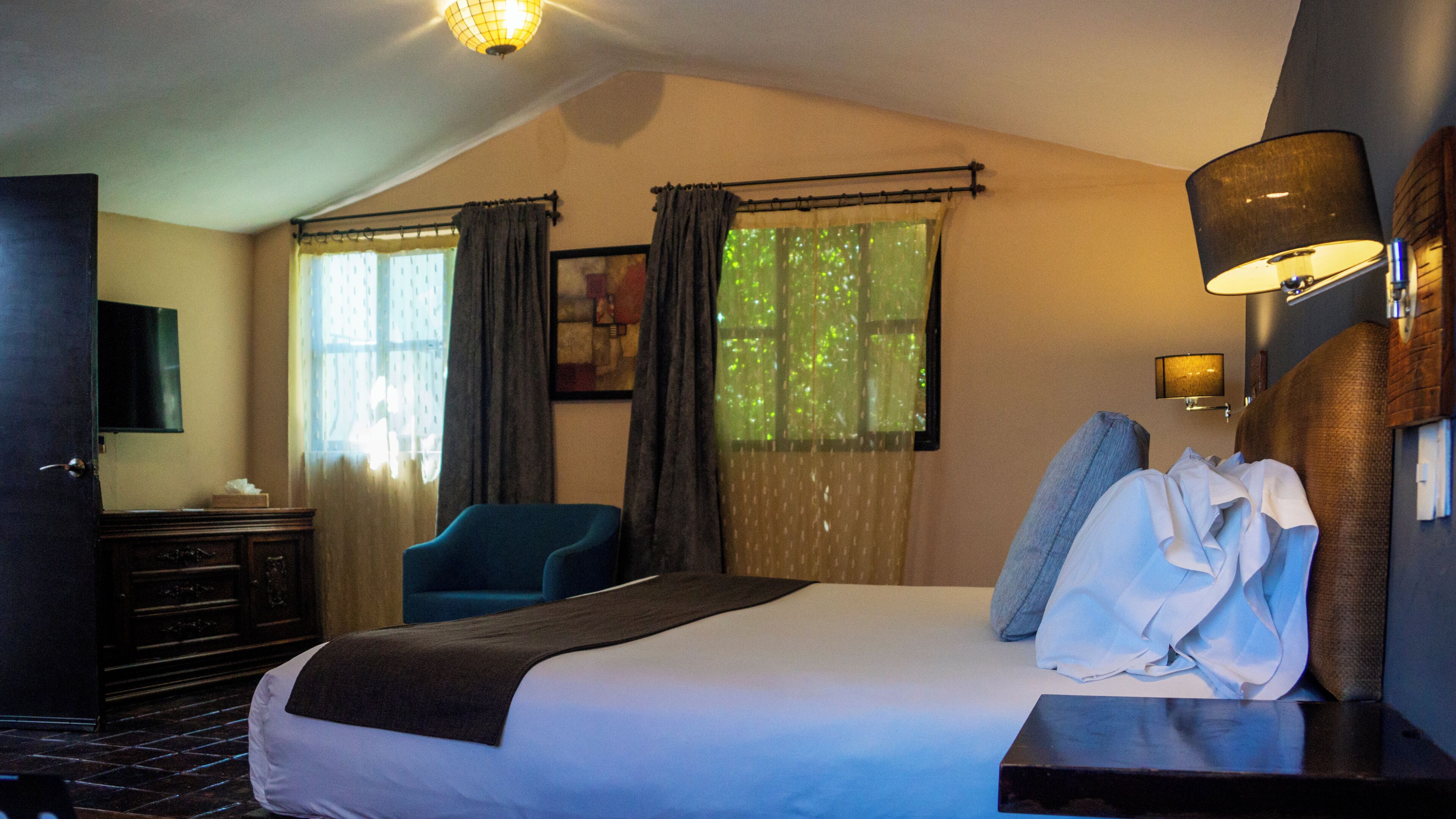 A hotel room with a bed, a desk, a chair, a TV, and a window with curtains.