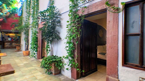 A courtyard with potted plants, a tiled floor, and a building entrance with a dark door. - Hotel Mesones 49 (San Miguel de Allende)