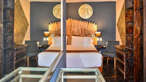 A modern hotel room with a large bed, two chairs, a desk, and a glass coffee table. - Hotel Mesones 49 (San Miguel de Allende)