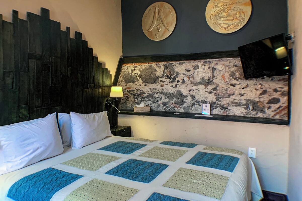 A hotel room with a large bed, a stone wall, and two wall-mounted decorative plates.