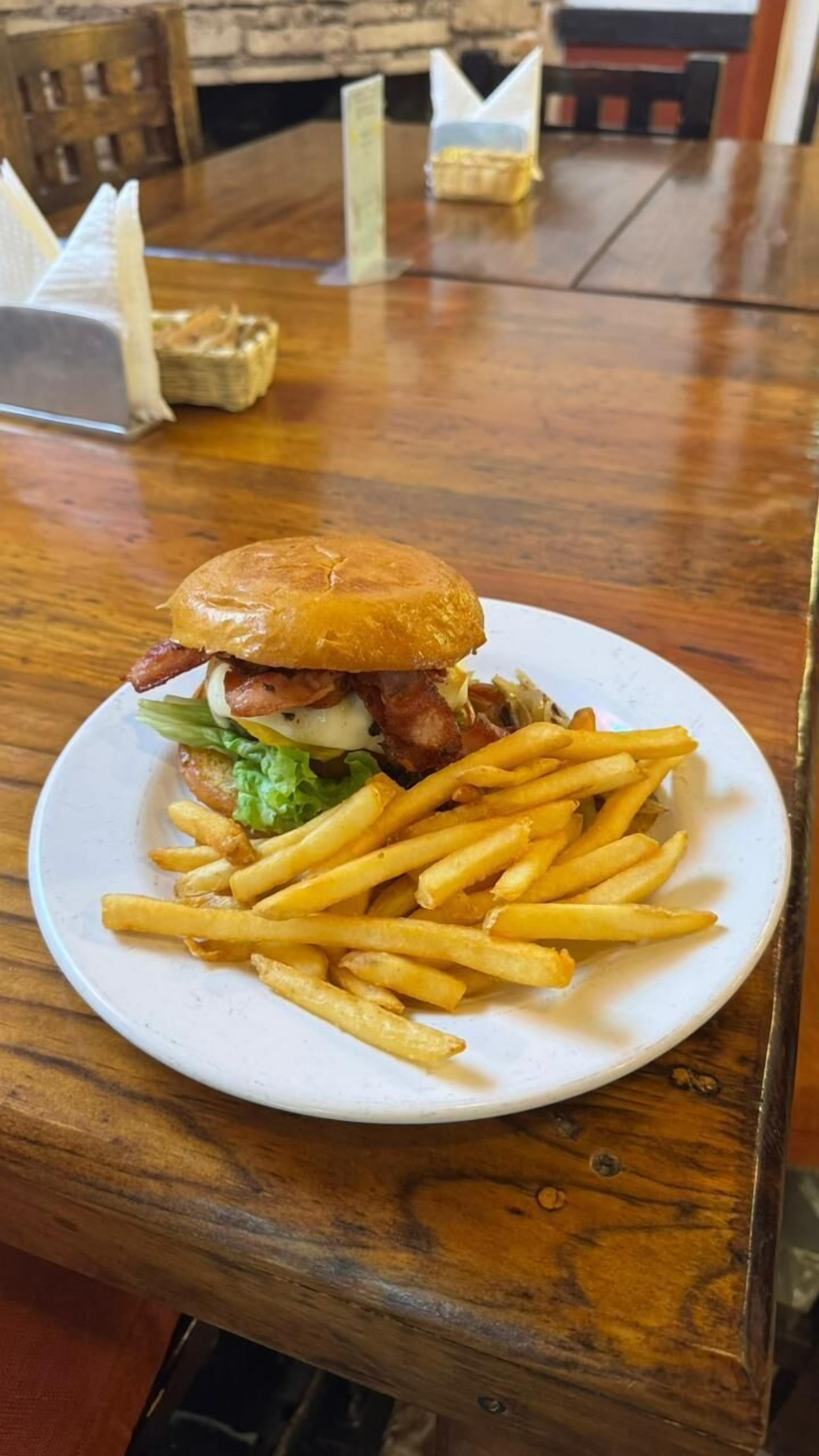 Un plato con una hamburguesa y papas fritas sobre una mesa de madera.