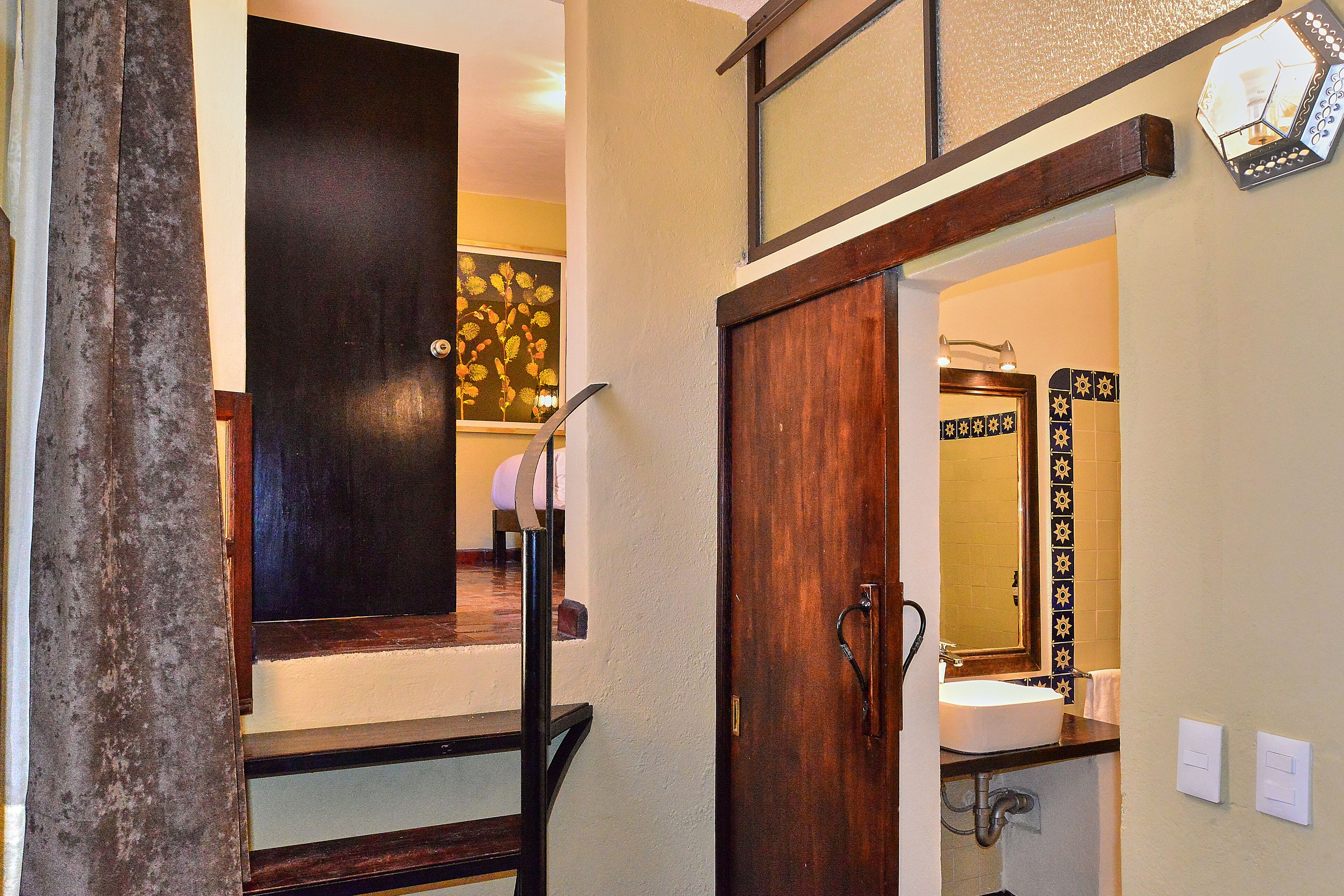 A bathroom with a wooden door, a sink, and a mirror with a decorative frame.