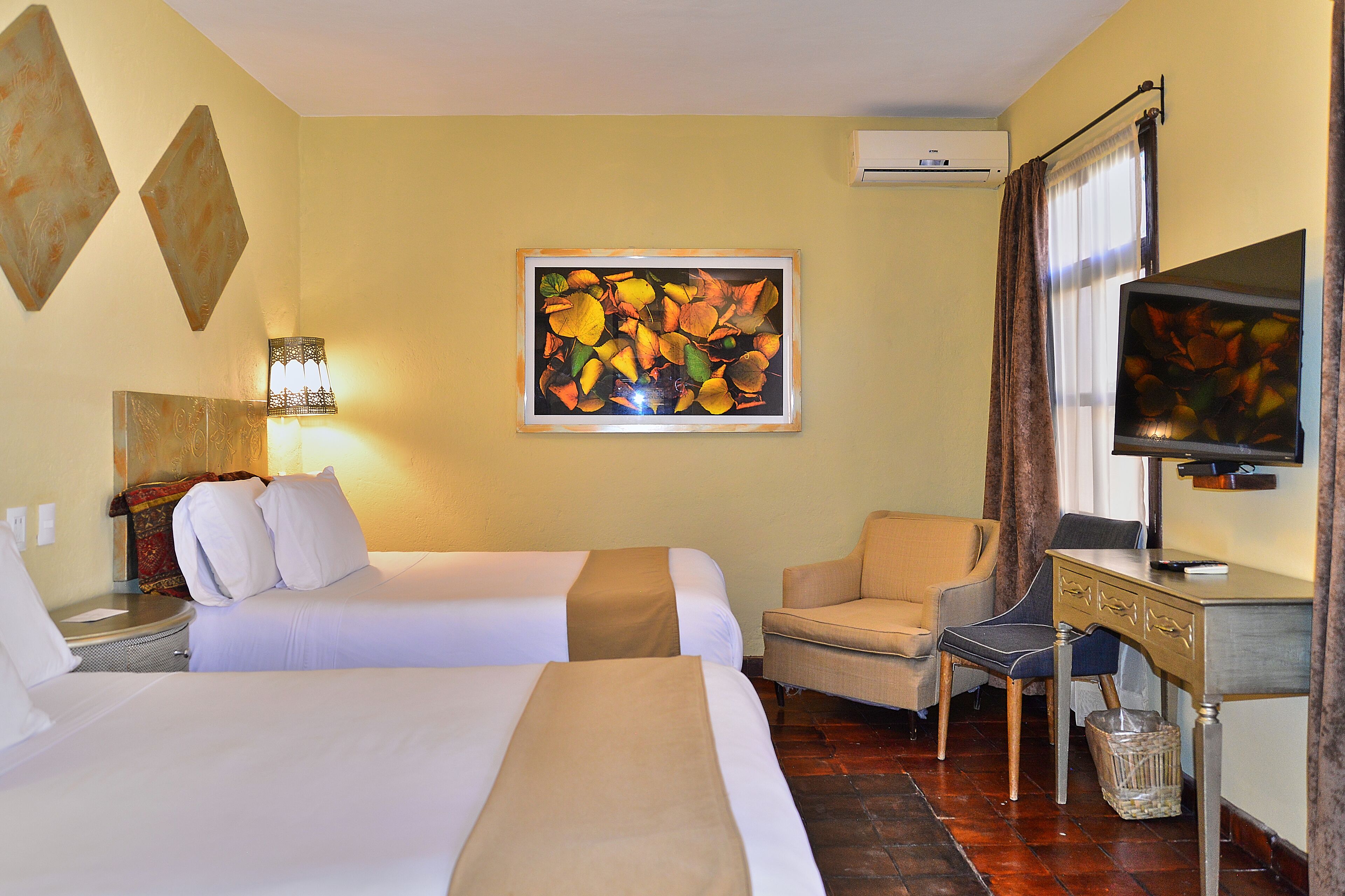 A hotel room with two beds, a desk with a chair, a television, and a painting on the wall.