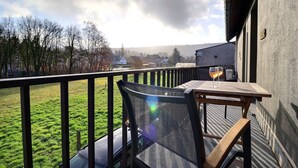 Ein Balkon mit Tisch und Stuhl, einem Weinglas und Blick auf ein Wiesenfeld sowie Häuser in der Ferne.