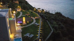 Ein Hotel an der Küste mit Pool, Liegestühlen und einem gut beleuchteten Garten.