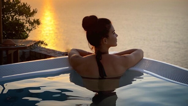 Eine Person entspannt in einem mit Sonnenlicht durchfluteten Infinity-Pool mit Blick auf den Sonnenuntergang.