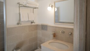 Ein Badezimmer mit einer beige gefliesten Wand, einem Waschbecken mit Spiegel darüber und einem Handtuchhalter mit Handtüchern.