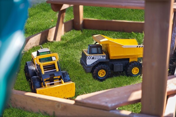 A model of a yellow construction vehicle with a cabin and a front loader, placed on a grassy surface. - Gated Heated Pool - Large Playset - Walk to Stadiums - 6 Beds (Arlington)